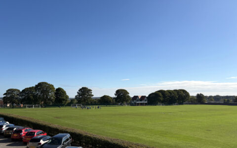 Queen Elizabeth’s Academy grounds in Mansfield with students enjoying outdoor PE on the green fields, framed by trees and the historic building on a sunny autumn day.